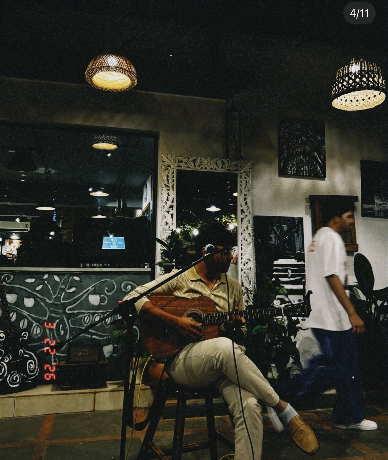 Musician playing guitar at night as someone walks past